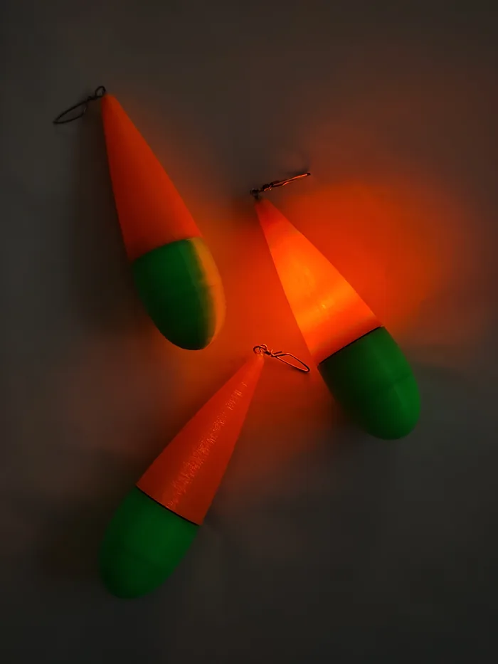 Tres boyas de pesca impresas en 3D encendidas en la oscuridad, con el cuerpo naranja iluminado desde adentro.