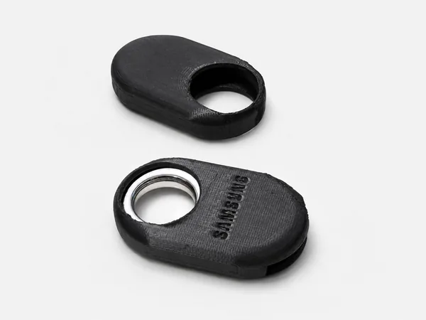 Protector impreso en 3D en negro para un Samsung SmartTag, abierto en sus dos mitades y con el dispositivo colocado.