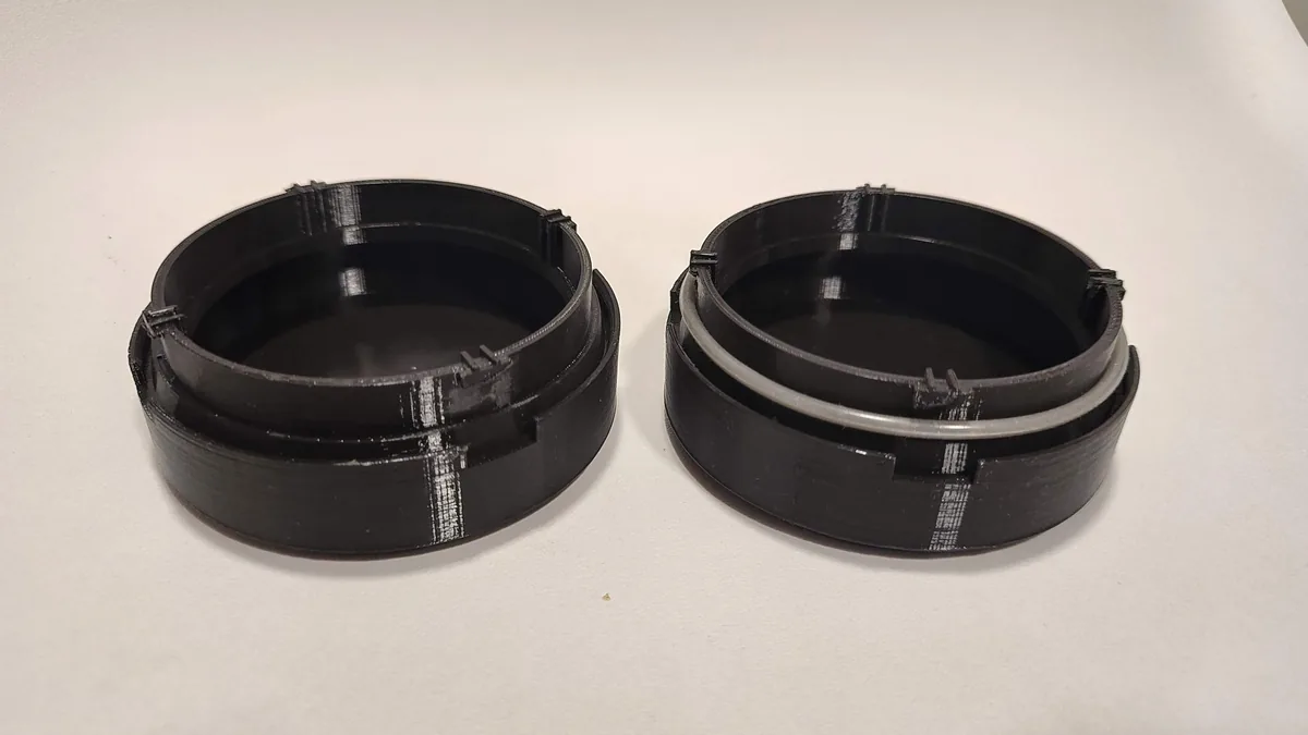 Dos tapas circulares negras impresas en 3D, una con su junta tórica colocada.